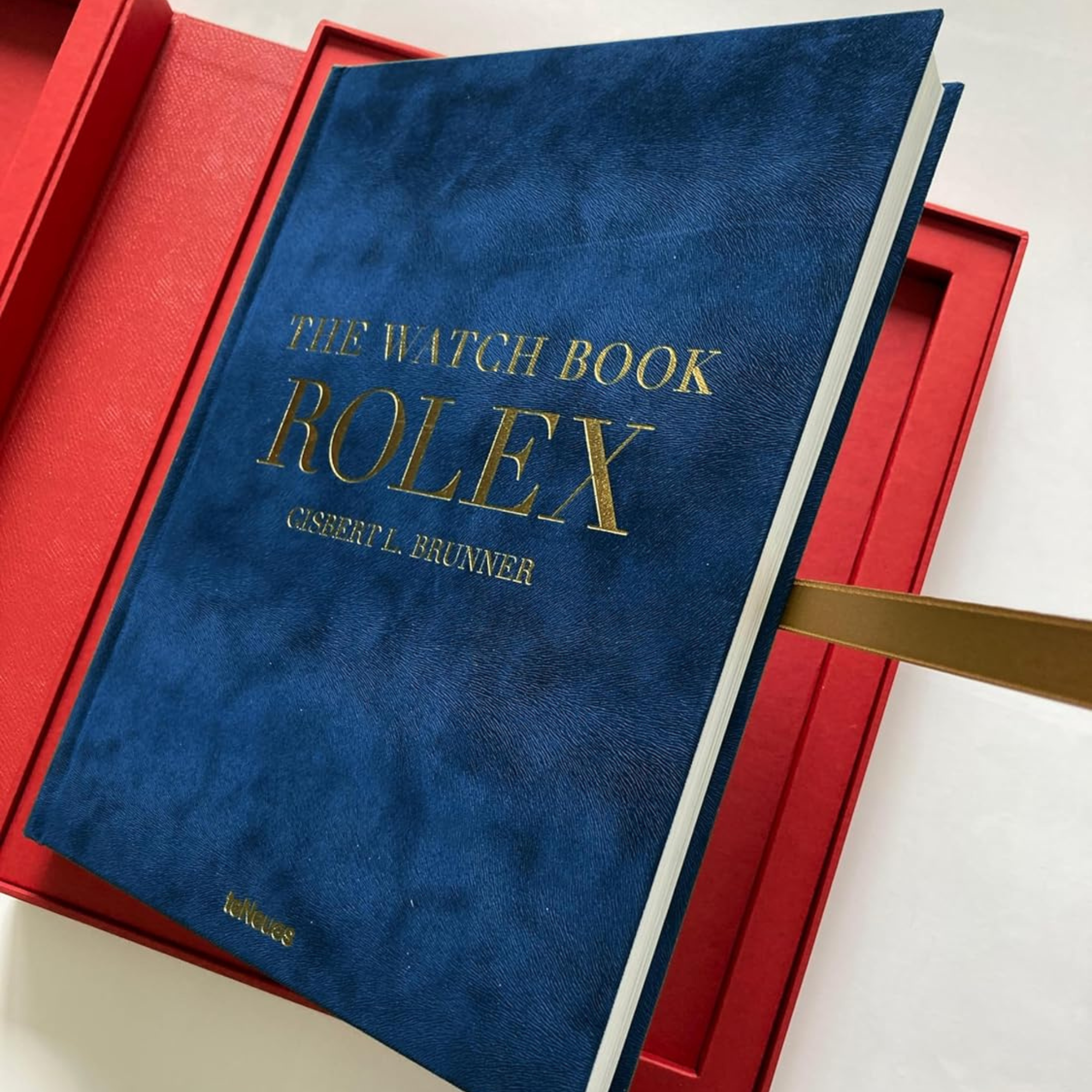 A luxury edition watch book titled 'THE WATCH BOOK ROLEX' by Teneues, featuring a blue cover with gold embossment and a red collector's box.