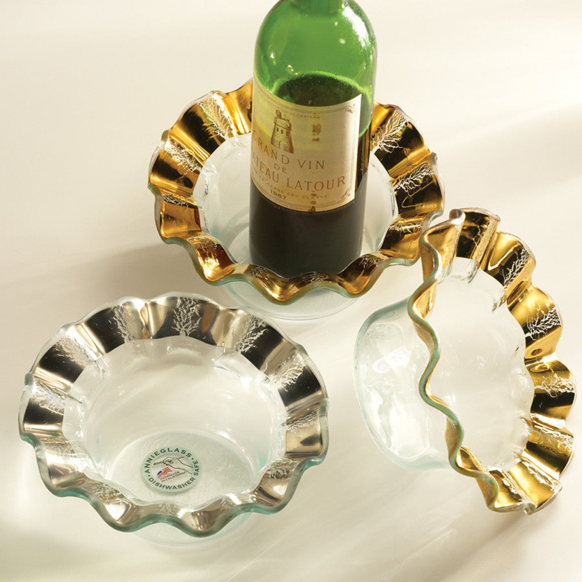 Gold and silver decorative bowls with a bottle of wine on a light background