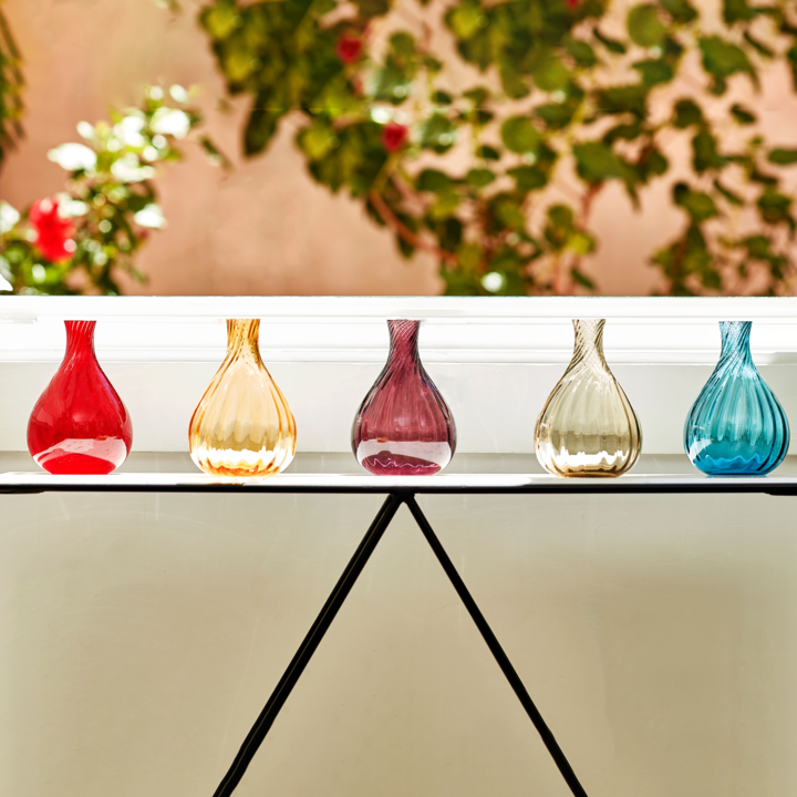 5 glass bud vases on a table -- red, orange, purple, gray, and blue